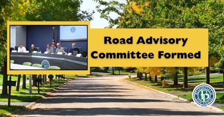 A road surrounded by trees with a picture of men setting at a desk and the works "road advisory committee formed" in front of it. 