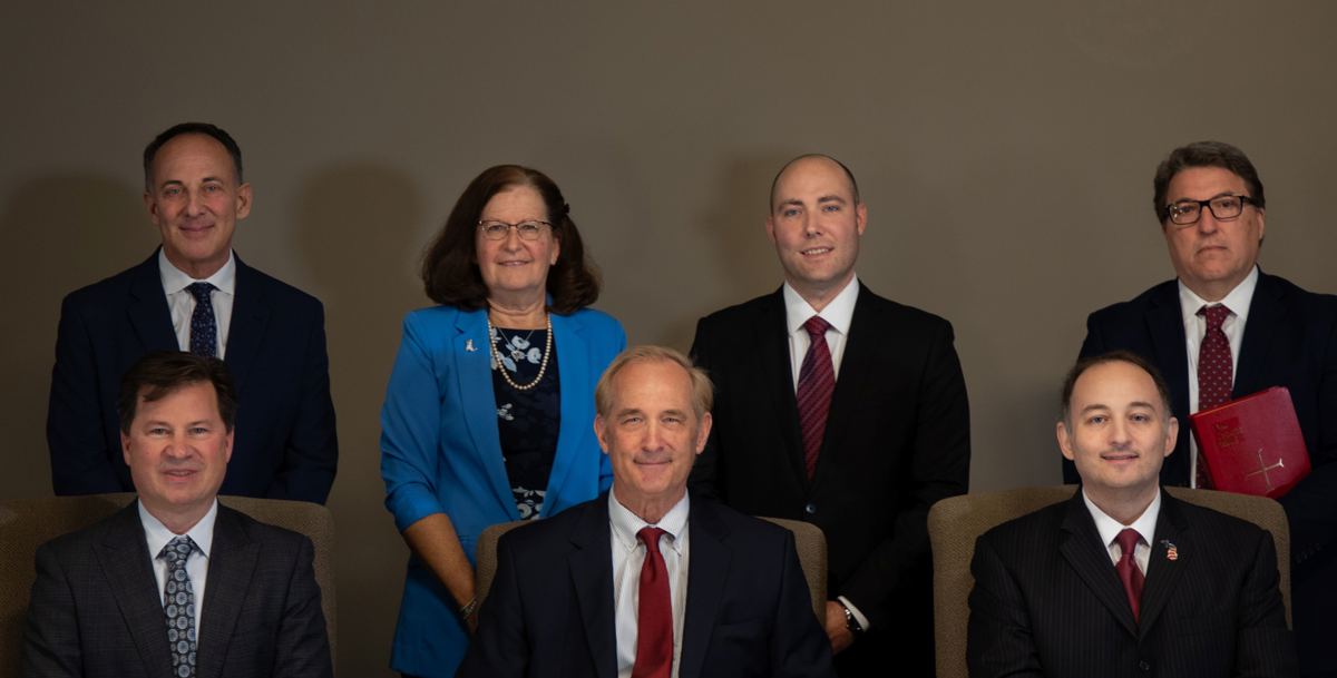 Three men sitting down with a woman and three other men standing behind them. All looking at the camera. 