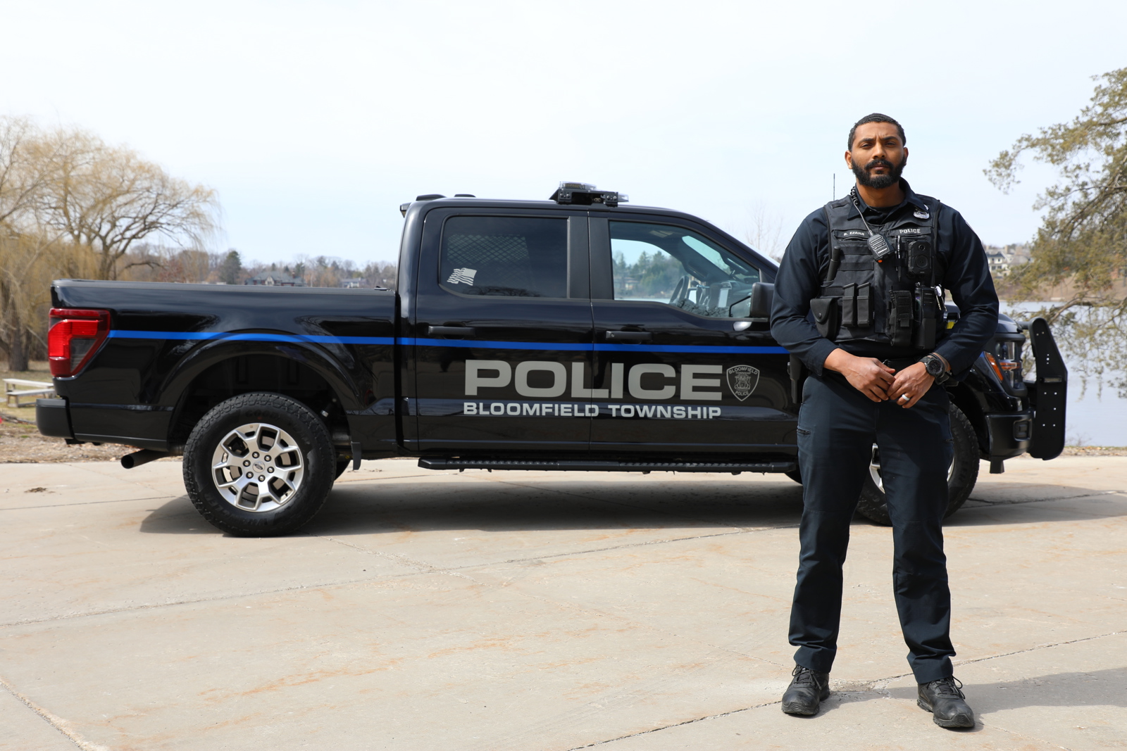 black male police officer taking commanding stance in front of side profile of police truck
