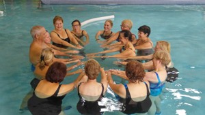 adults in a pool standing in a circle with arms into the center of the circle.