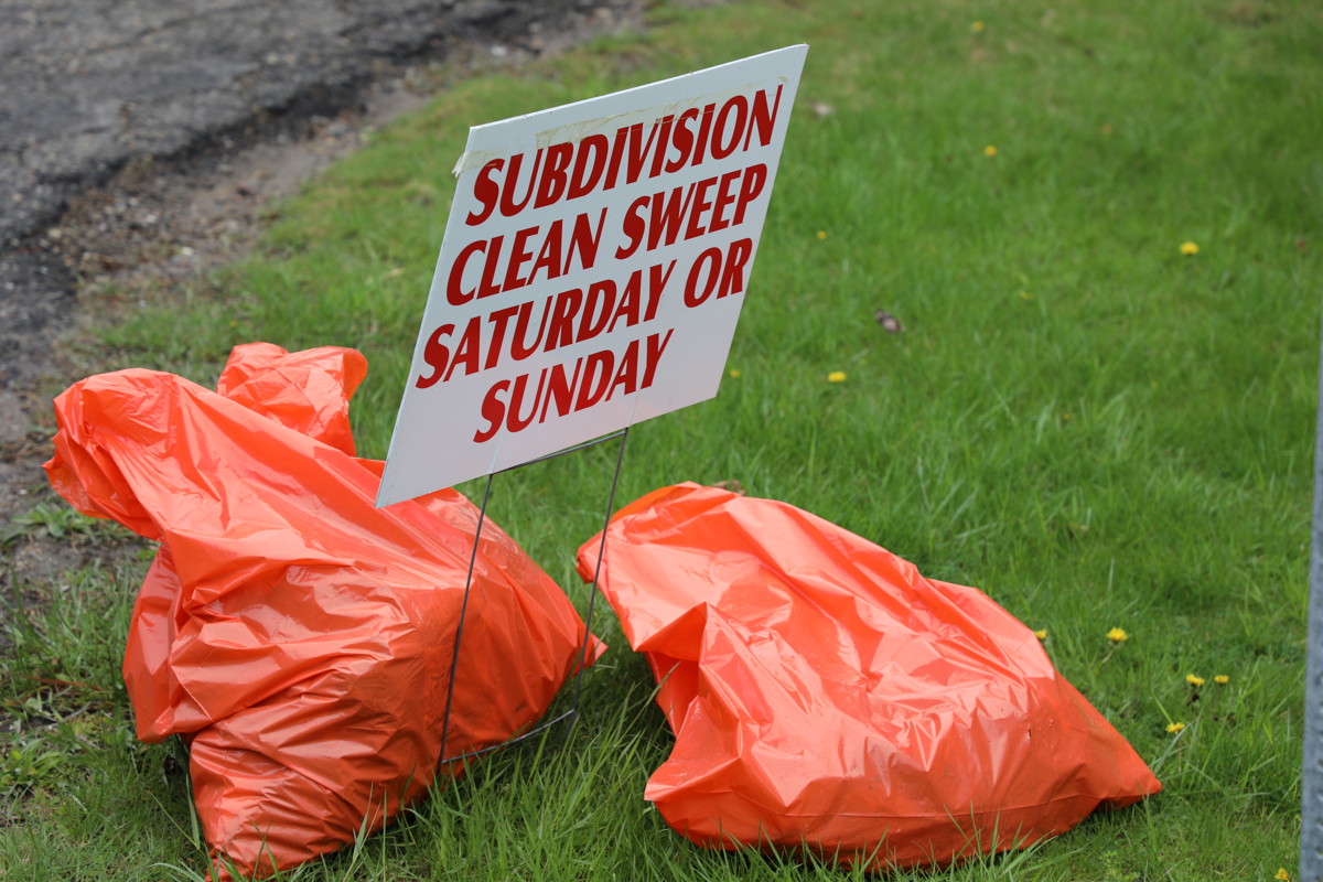 Orange trash bags on grass with lawn sign that reads Subdivision Clean Sweep Saturday or Sunday