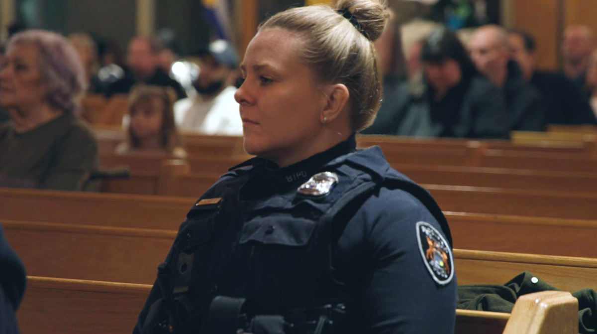 A woman police officer sitting in a wooden pew. 