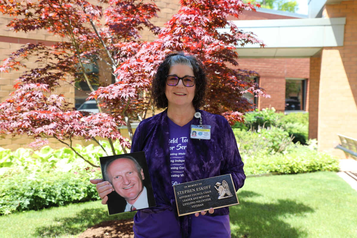 A woman standing outside holding a plaque and a picture of a man. 