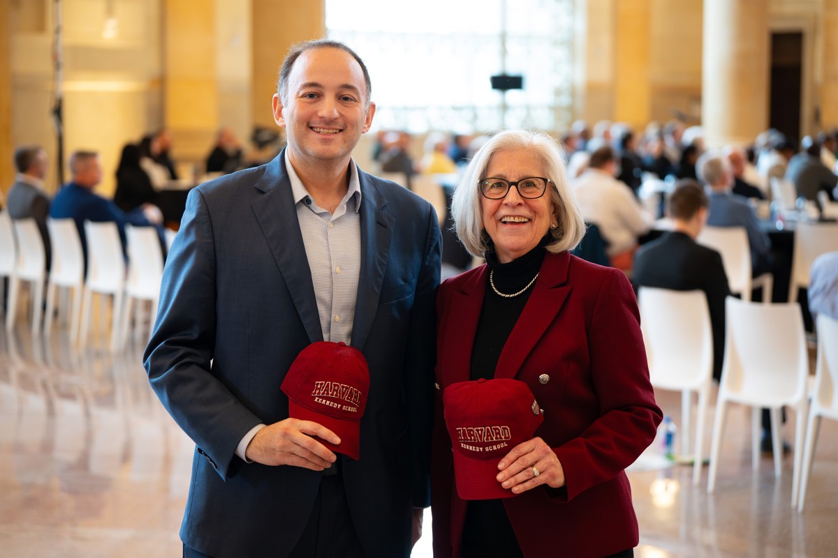 A woman and a man holding Harvard hats next to each other. 