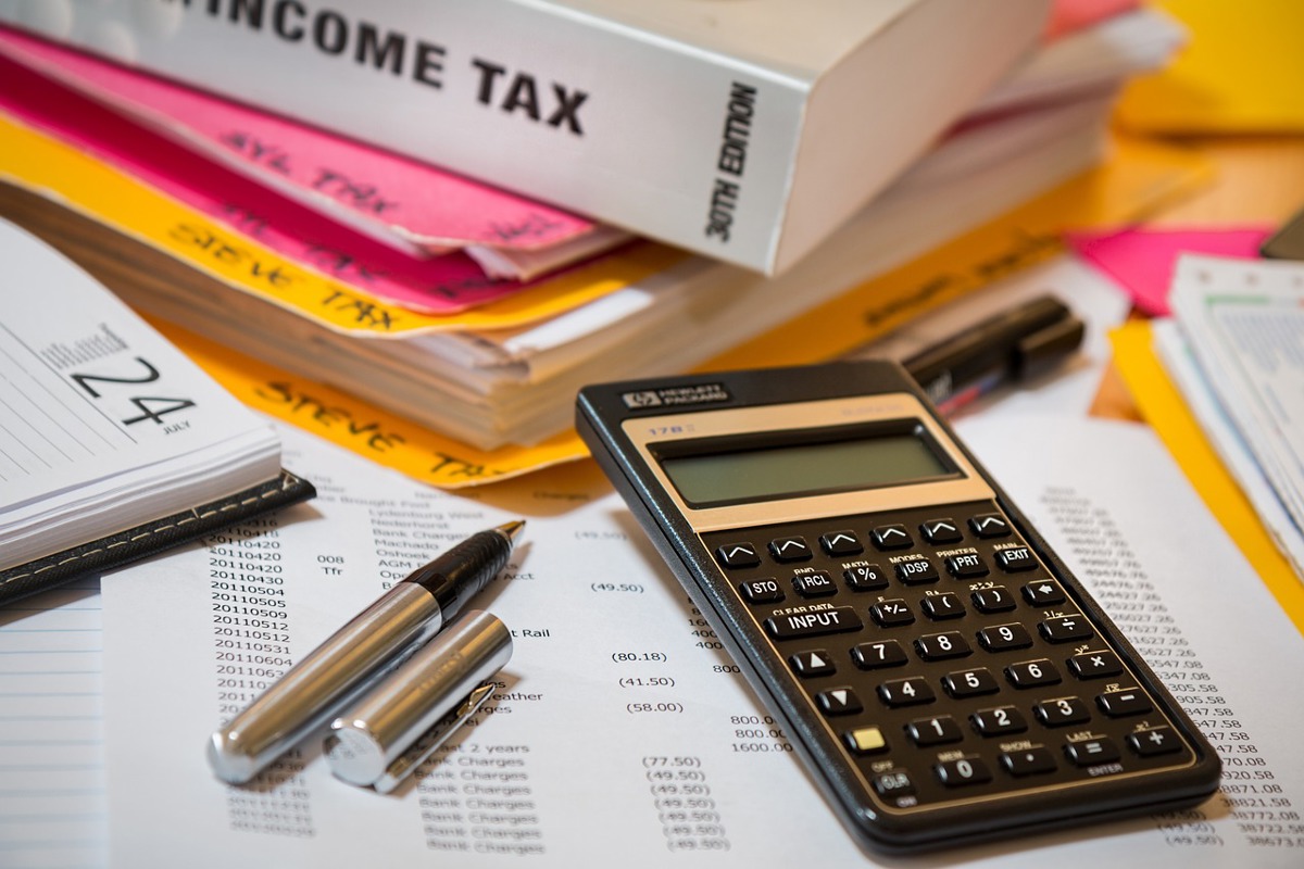 Calculator sitting on financial information with an uncapped pen to the left of it. 