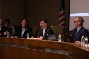Clerk Martin Brook speaking at microphone while seated at dais with other Township Trustees looking on.