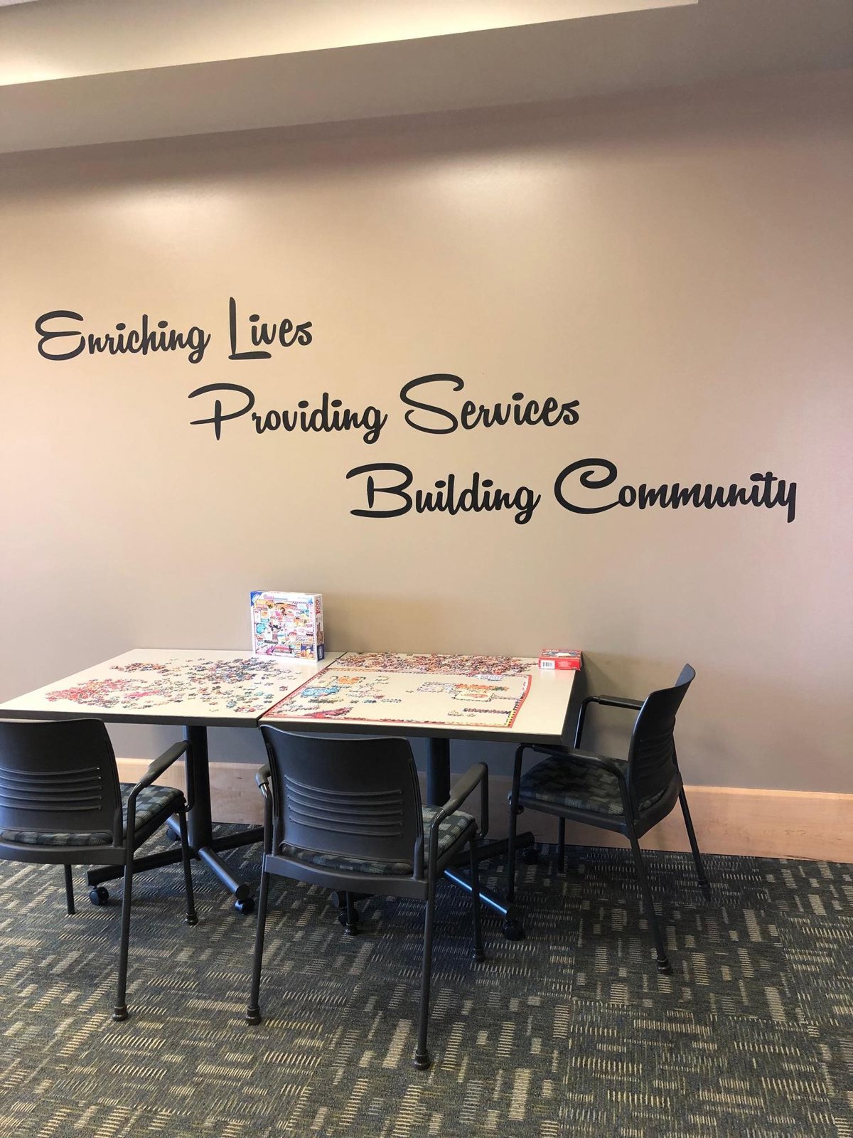 Table with three chairs around it. The words "Enriching lives, providing services, building community" on the wall above. 