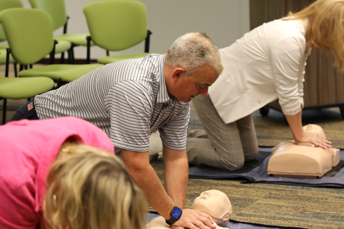 Three people on their knees practicing CPR on dummies that are lying on the floor.