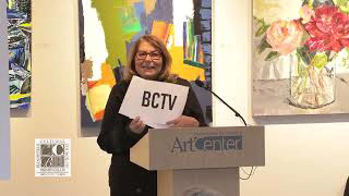 A woman standing at a podium holding a BCTV sign. 