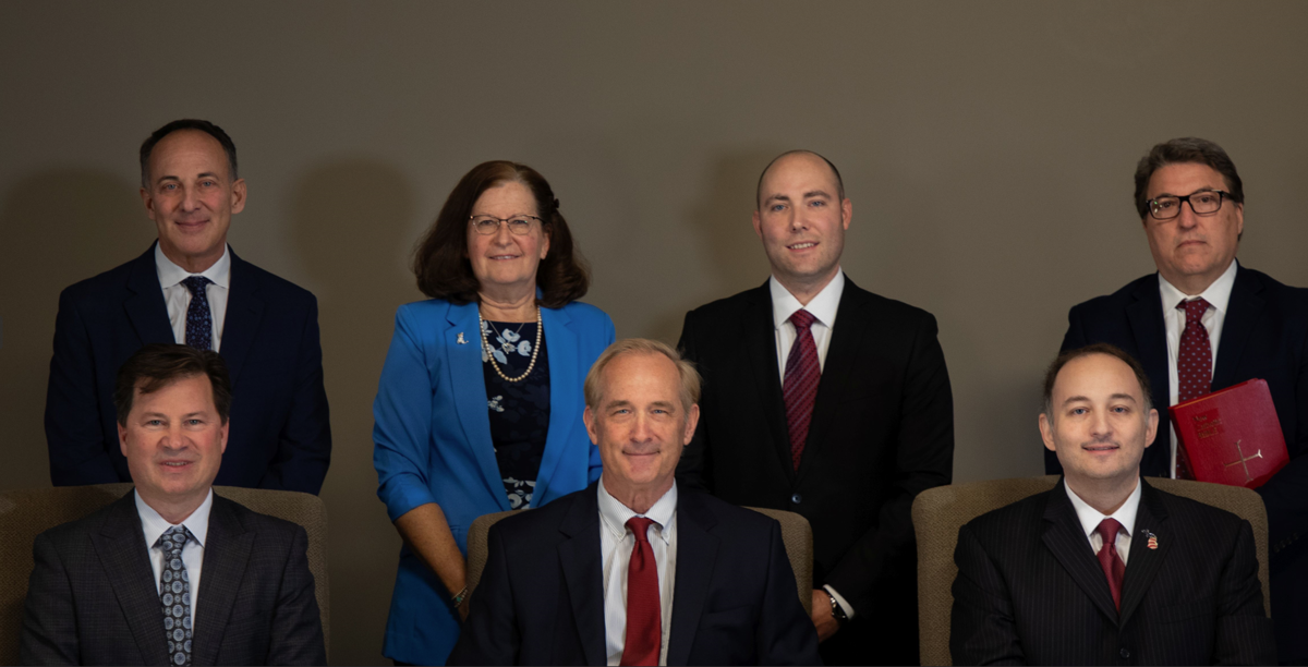 Three men sitting and looking at the camera with three men and one woman standing behind them. 